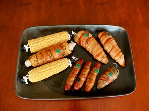 Image of a platter of corn and meat, Grill Pinz being used to wrap bacon for yummy eating.